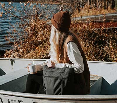 Girl drinking coffee in branded hat while sitting in a boat