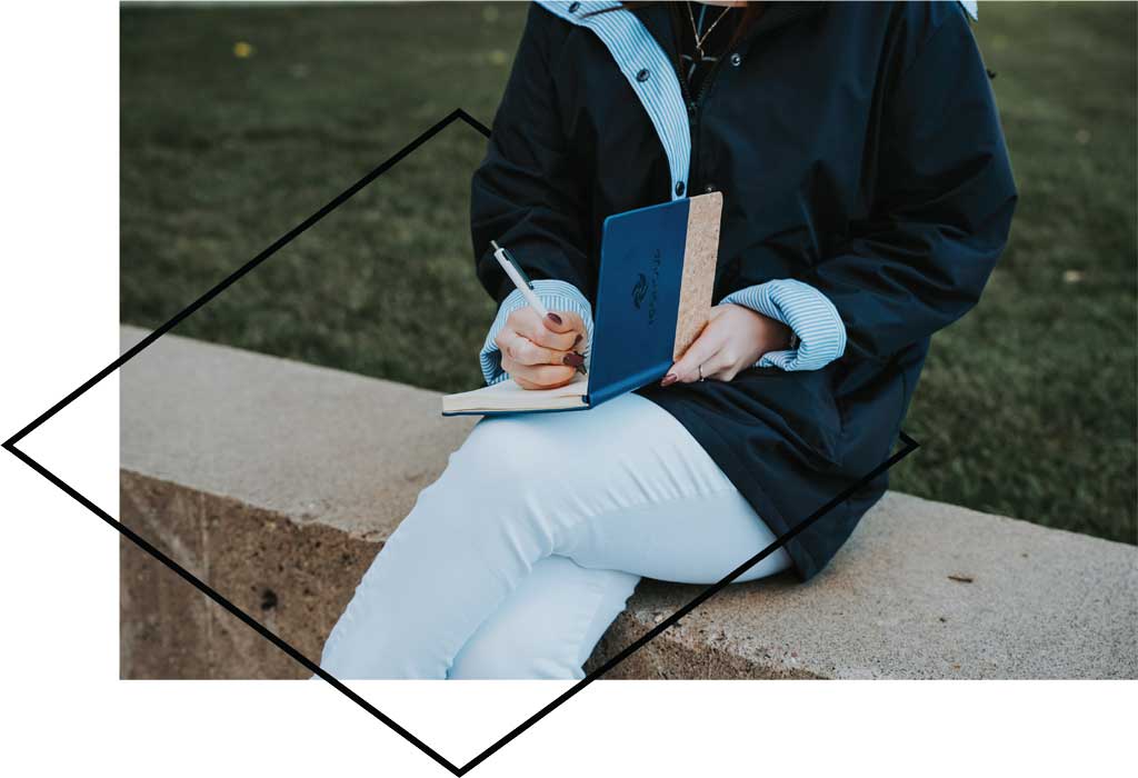 Person sitting outside writing in branded notebook