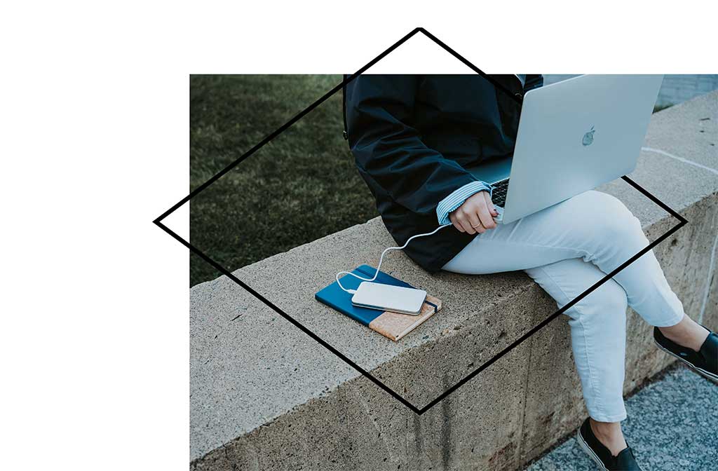 Woman sitting outside on cement divider working on laptop