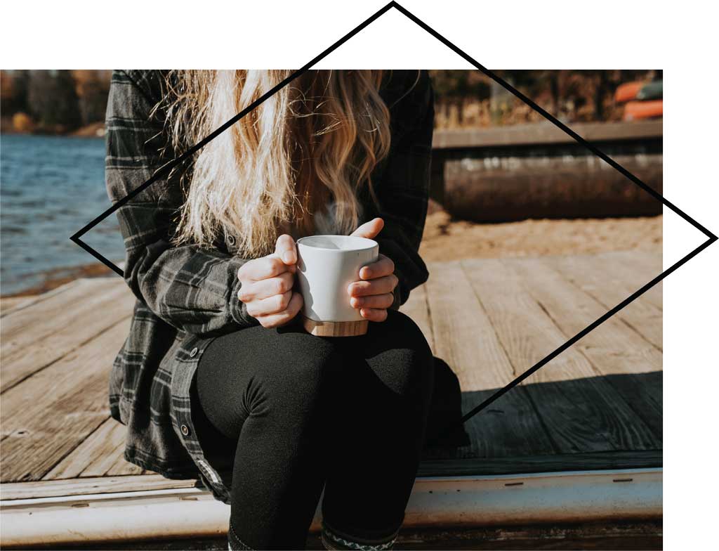 Young woman sitting on dock drinking coffee